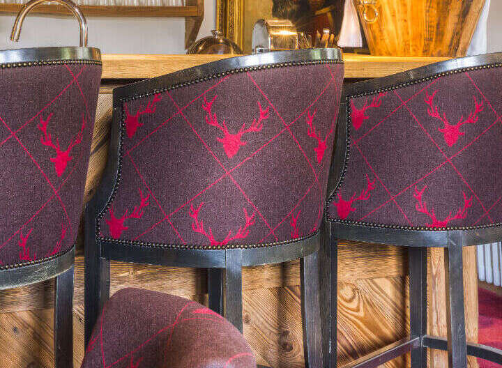 Experience rustic elegance in this charming bar area, featuring plush bar stools upholstered in a rich, dark fabric with a distinctive red stag pattern.