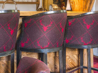 Experience rustic elegance in this charming bar area, featuring plush bar stools upholstered in a rich, dark fabric with a distinctive red stag pattern.