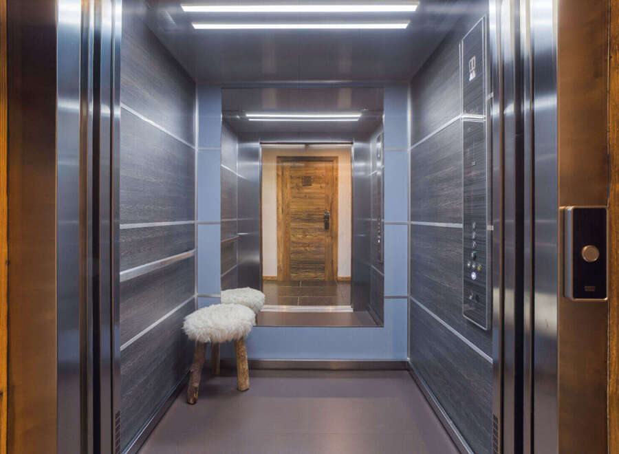 Step into this luxurious elevator, featuring a modern design with dark wood-paneled walls and sleek stainless steel accents.