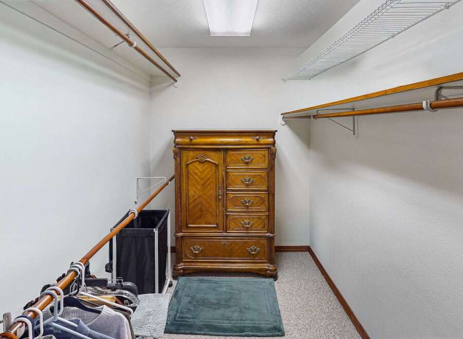 Step into this spacious walk-in closet, offering ample storage with its built-in shelving and a classic wooden dresser.