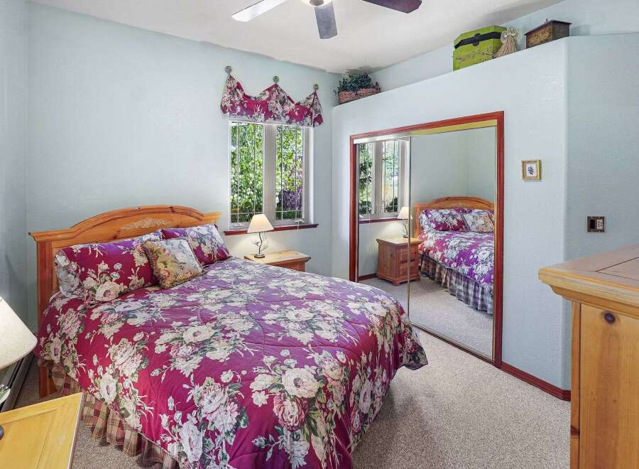 This charming bedroom features a cozy queen-sized bed adorned with a vibrant floral comforter, creating a warm and inviting atmosphere.