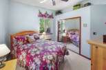 This charming bedroom features a cozy queen-sized bed adorned with a vibrant floral comforter, creating a warm and inviting atmosphere.