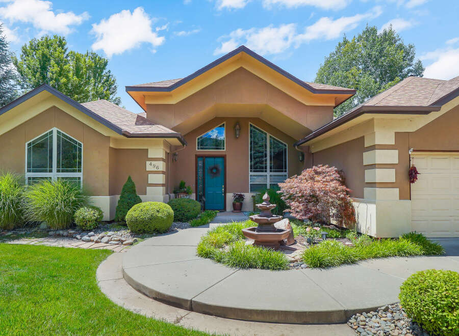 Welcome to this stunning home featuring a striking teal front door and a charming tiered fountain in the landscaped front yard.