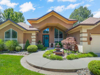 Welcome to this stunning home featuring a striking teal front door and a charming tiered fountain in the landscaped front yard.
