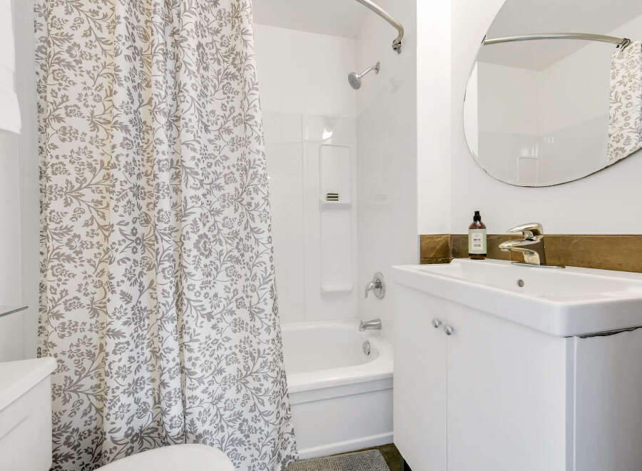 This bright bathroom features a clean, modern design with a white vanity and a stylish, floral-patterned shower curtain.