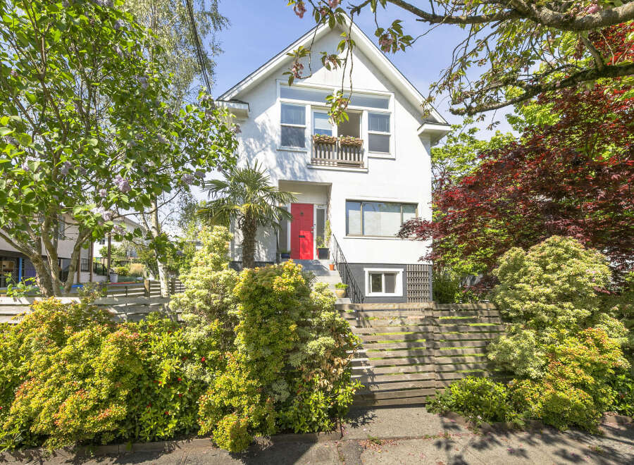 Charming two-story home with a vibrant red front door, nestled amidst lush greenery.