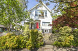 Charming two-story home with a vibrant red front door, nestled amidst lush greenery.