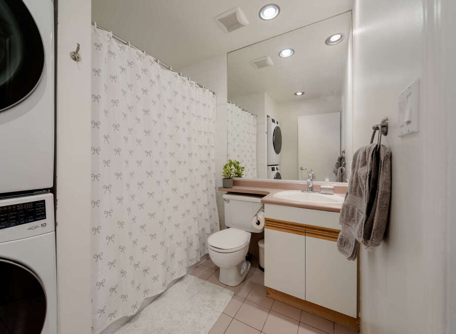 This well-appointed bathroom features a modern design with a convenient stacked washer and dryer.