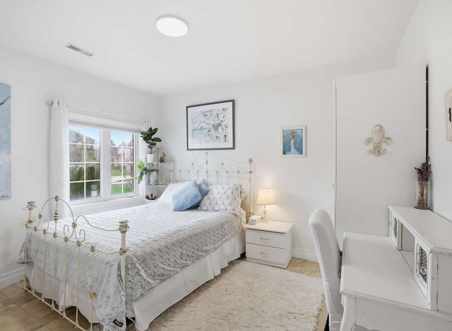 This charming bedroom offers a serene retreat with its elegant white decor and ample natural light.