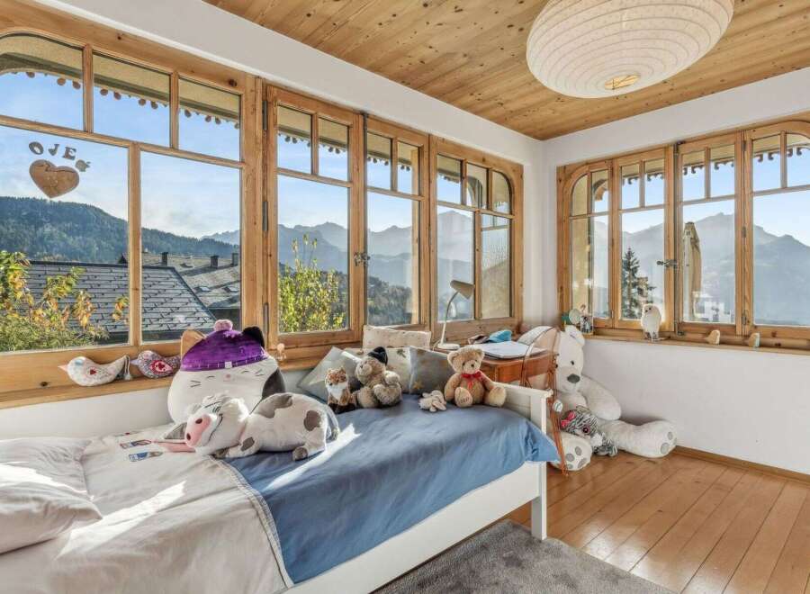 Experience the charm of this cozy bedroom, boasting stunning mountain views framed by elegant wooden windows.