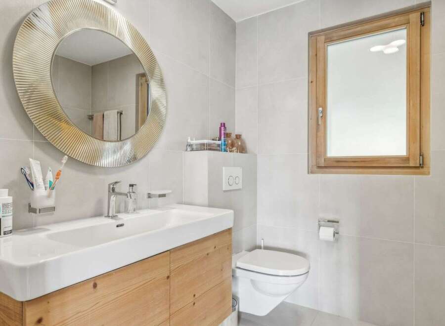 This modern bathroom features a stylish round mirror, a sleek white sink, and a wooden vanity, creating a clean and inviting space.