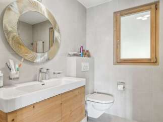 This modern bathroom features a stylish round mirror, a sleek white sink, and a wooden vanity, creating a clean and inviting space.