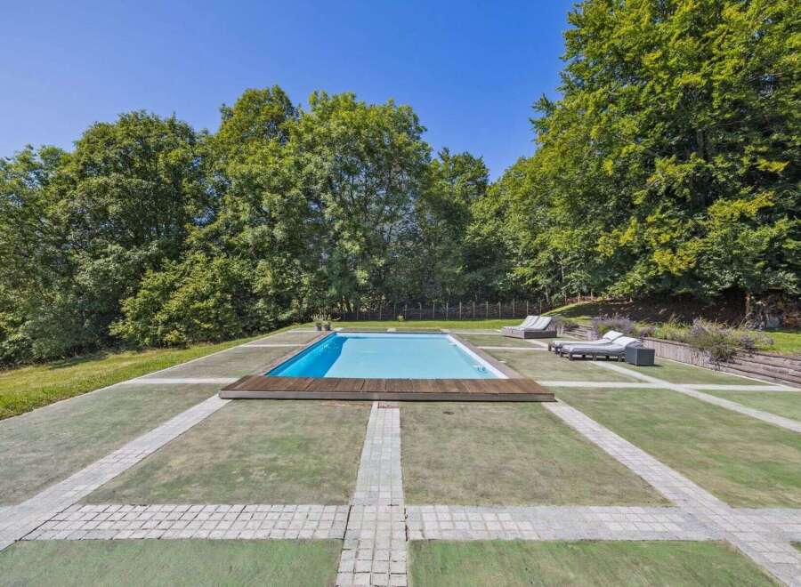 Enjoy luxurious outdoor living with this stunning property featuring a pristine swimming pool surrounded by lush greenery.