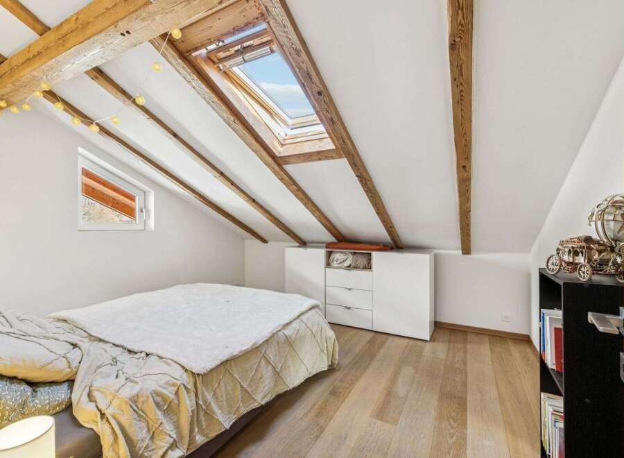 This charming attic bedroom boasts a unique architectural design with exposed wooden beams and a skylight that floods the space with natural light.