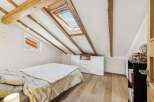 This charming attic bedroom boasts a unique architectural design with exposed wooden beams and a skylight that floods the space with natural light.