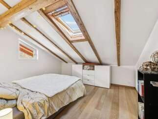 This charming attic bedroom boasts a unique architectural design with exposed wooden beams and a skylight that floods the space with natural light.