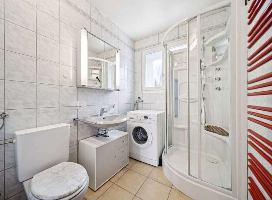 This well-maintained bathroom features a modern design with a washing machine, a shower, and a toilet.