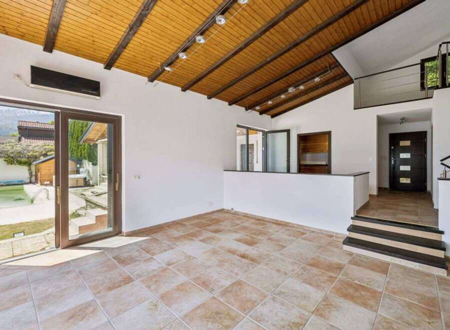 Experience modern living in this spacious room featuring a vaulted wooden ceiling with exposed beams and track lighting.