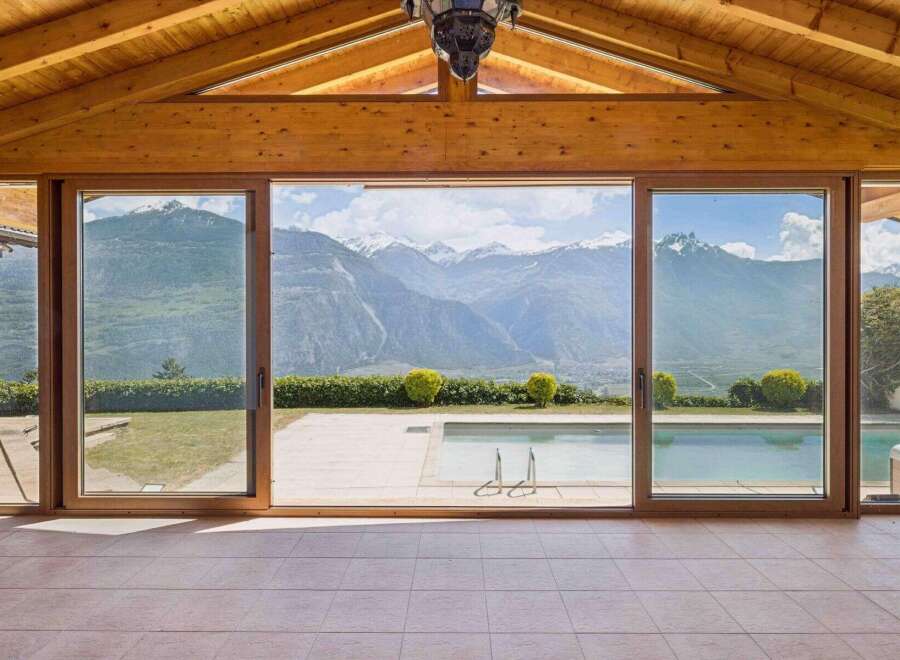 Experience breathtaking mountain views from this stunning property, featuring expansive glass doors that open to a pristine swimming pool and a lush green landscape.