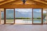 Experience breathtaking mountain views from this stunning property, featuring expansive glass doors that open to a pristine swimming pool and a lush green landscape.