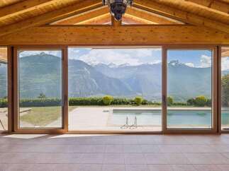 Experience breathtaking mountain views from this stunning property, featuring expansive glass doors that open to a pristine swimming pool and a lush green landscape.