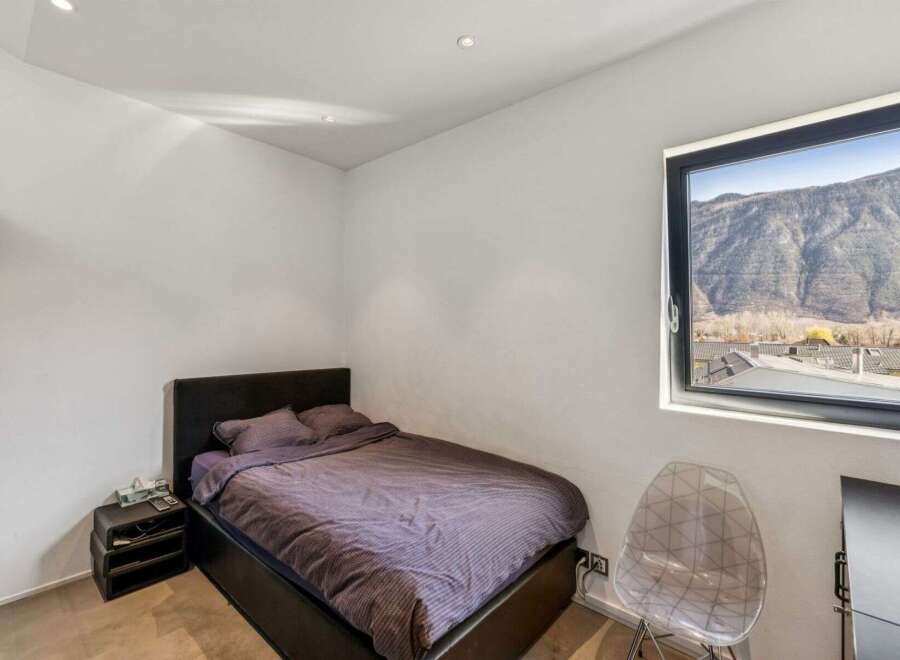 Discover the tranquility of this modern bedroom, featuring a comfortable bed and a stunning mountain view from the large window.