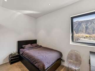 Discover the tranquility of this modern bedroom, featuring a comfortable bed and a stunning mountain view from the large window.