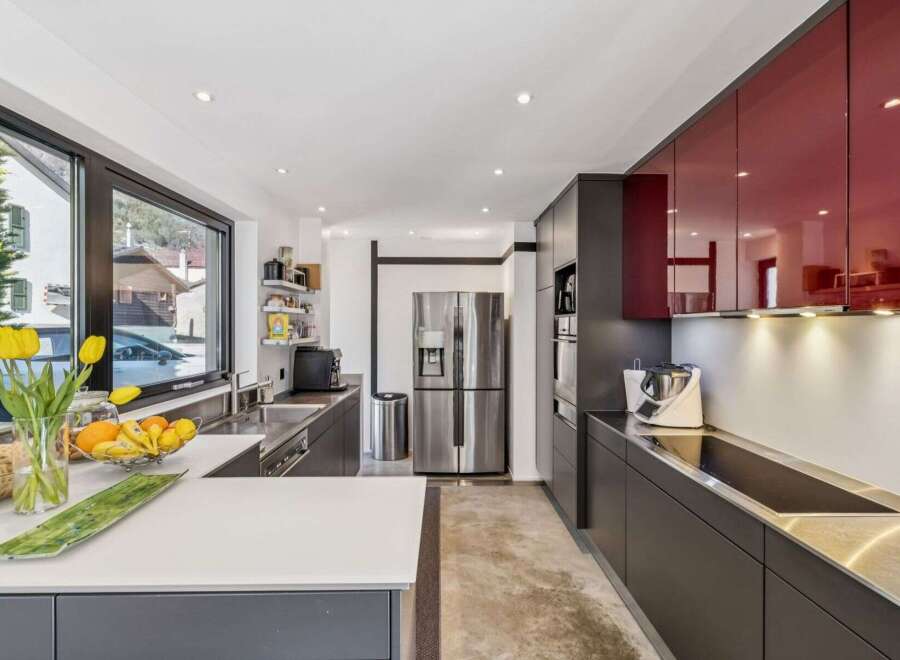 This modern kitchen boasts sleek, dark cabinetry and striking red upper cabinets, creating a sophisticated contrast.