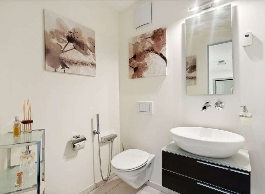 This modern bathroom features a sleek design with a floating toilet and a stylish vessel sink.