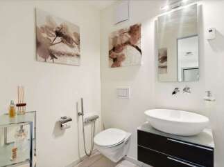 This modern bathroom features a sleek design with a floating toilet and a stylish vessel sink.