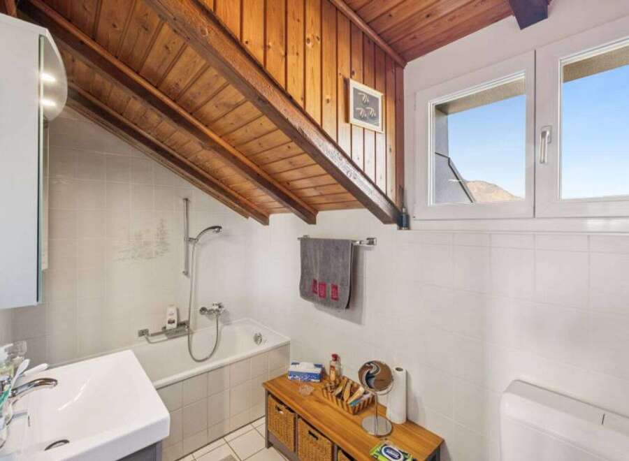 This charming bathroom features a unique sloped wooden ceiling, adding character and warmth to the space.