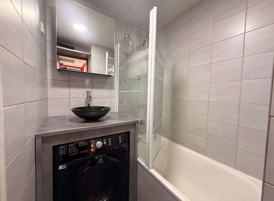 Discover this modern bathroom featuring a sleek black washing machine and a stylish vessel sink.