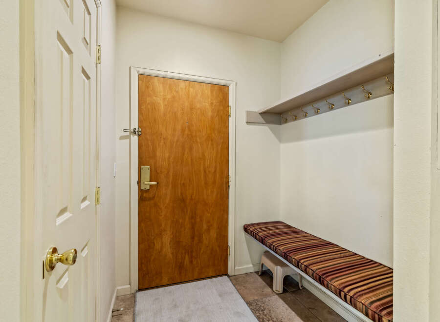 Step into this inviting entryway, featuring a warm wooden door and a convenient bench with striped cushions.