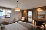 Experience mountain living in this cozy bedroom featuring a comfortable bed, rustic wooden walls, and a stunning view of snow-capped peaks through the large window.