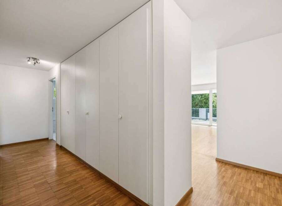 This bright and airy hallway features beautiful hardwood floors and a series of built-in white cabinets, offering ample storage space.