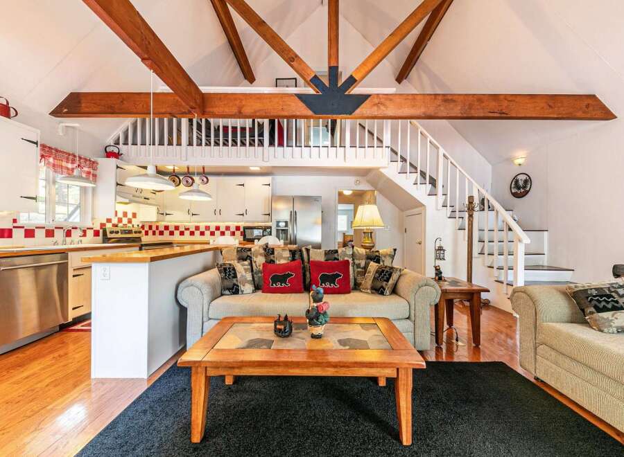 This charming cabin-style home boasts a cozy living area with a loft and exposed wooden beams, creating a warm and inviting atmosphere.