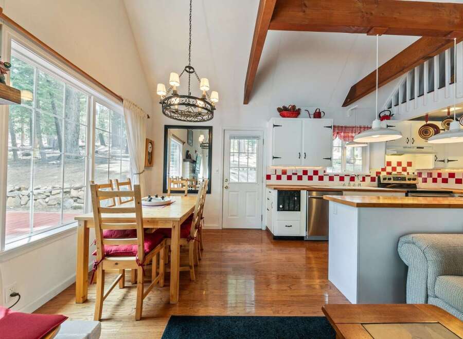 This charming kitchen and dining area boasts a cozy atmosphere with its wooden floors, exposed beams, and a stylish chandelier.