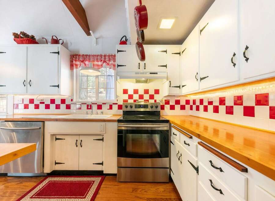 Step into this charming kitchen, featuring a classic design with white cabinetry and a striking red and white checkered backsplash.