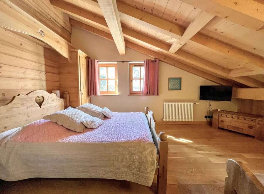 Discover the charm of this cozy bedroom featuring a rustic wooden bed frame and exposed beams, creating a warm and inviting atmosphere.