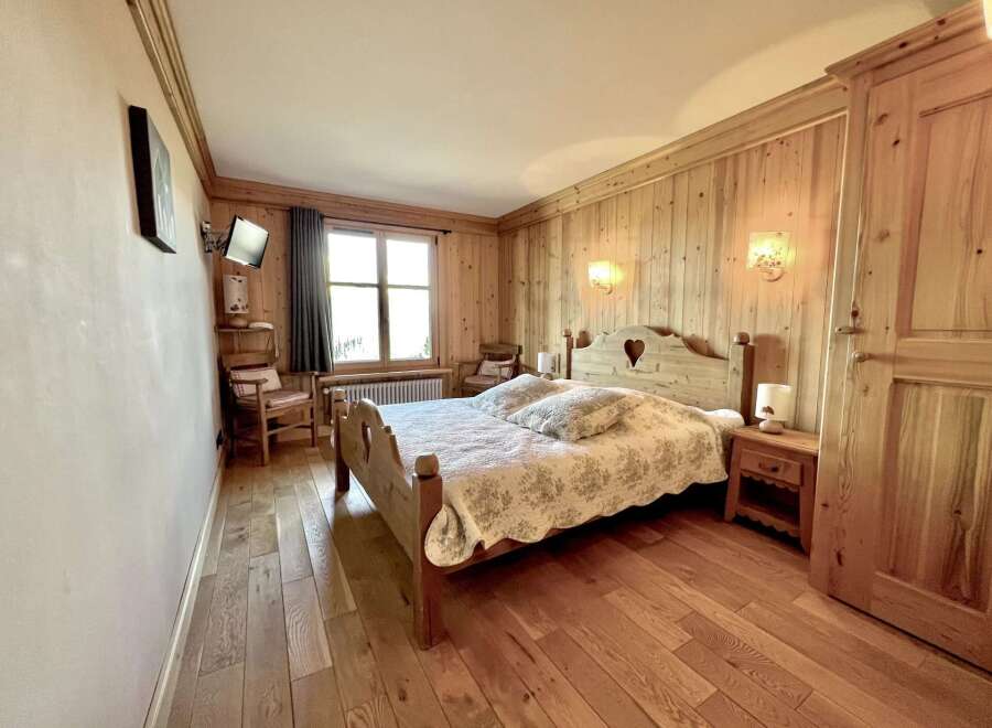 This charming bedroom features a cozy wooden bed frame with a heart-shaped cutout, complemented by matching wooden paneling and flooring.