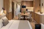 Discover modern living in this beautifully designed studio apartment, featuring a cozy sleeping area and a fully equipped kitchenette with sleek wooden cabinetry.