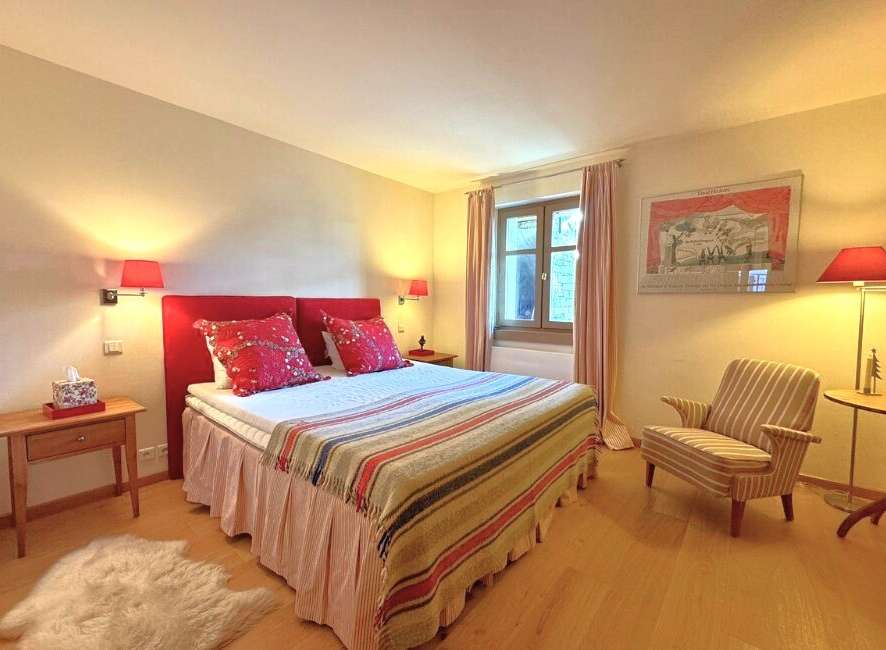 This cozy bedroom features a comfortable bed with a vibrant red headboard and decorative pillows, creating a warm and inviting atmosphere.