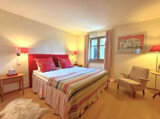 This cozy bedroom features a comfortable bed with a vibrant red headboard and decorative pillows, creating a warm and inviting atmosphere.