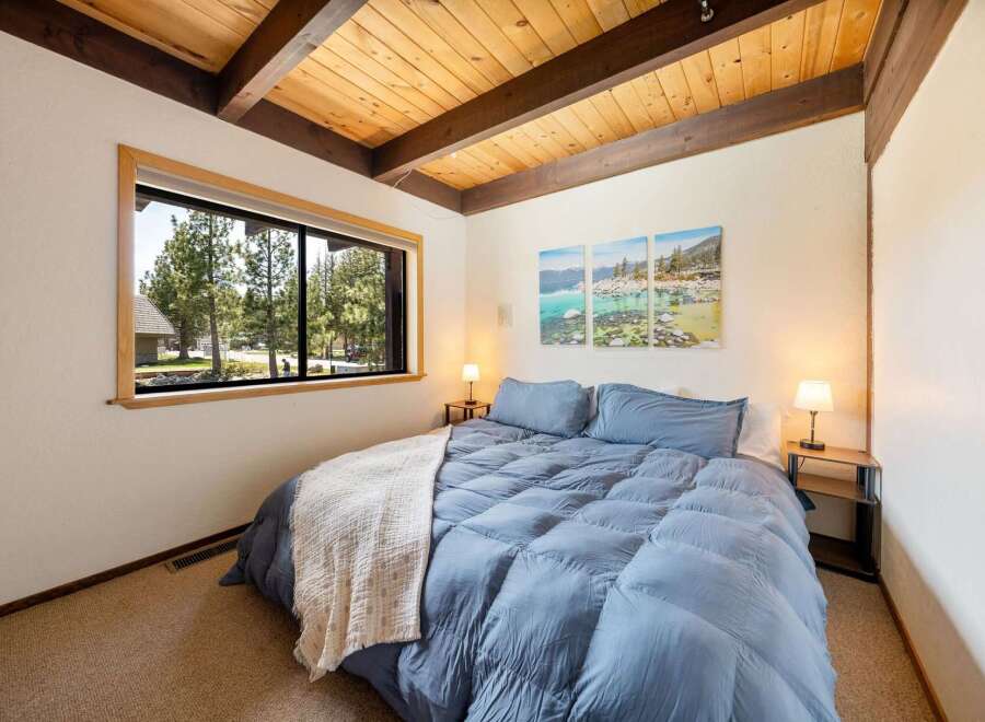 This cozy bedroom features a stunning wooden ceiling and a large window that offers a beautiful view of the surrounding trees.