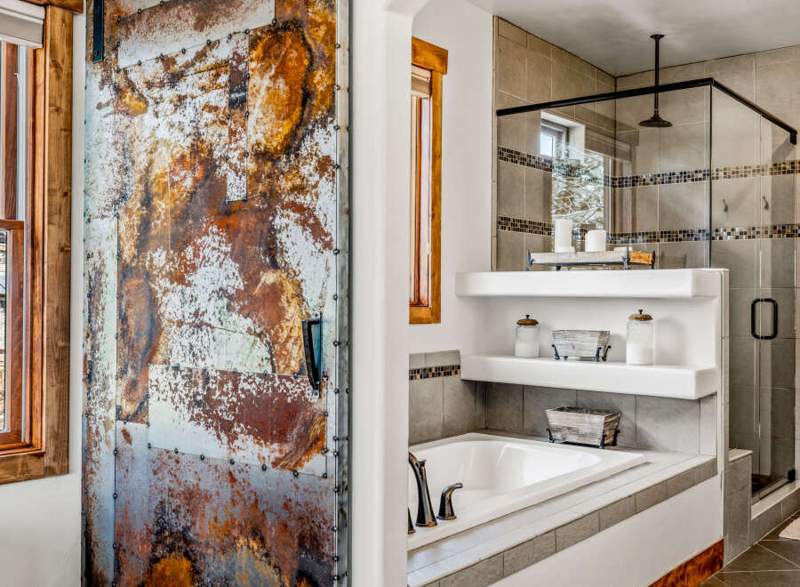 Step into luxury with this stunning bathroom featuring a unique, rustic metal door that adds a touch of industrial charm.