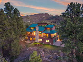 Nestled in a serene mountain setting, this stunning property boasts a luxurious multi-story home with a striking green roof.