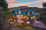 This stunning mountain home boasts a unique design with a green metal roof and a stone chimney, offering a blend of rustic charm and modern elegance.