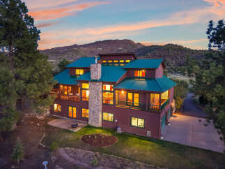 This stunning mountain home boasts a unique design with a green metal roof and a stone chimney, offering a blend of rustic charm and modern elegance.
