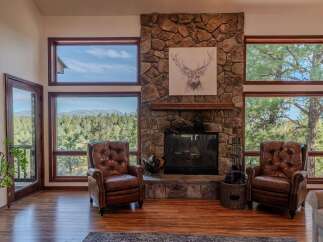 Experience breathtaking mountain views from this stunning living room, featuring a grand stone fireplace and expansive windows.