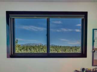 Experience breathtaking views from this stunning property, featuring a large window that frames a picturesque landscape of lush green forests and majestic mountains under a clear blue sky.